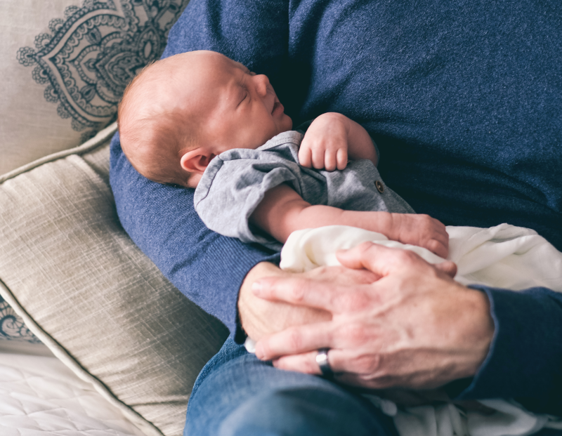 father in a blue sweater holding a newborn baby