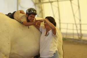 A child laying on top of a horse is assisted by an instructor