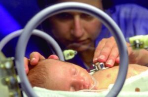A nurse presses a stethoscope to a baby's chest.